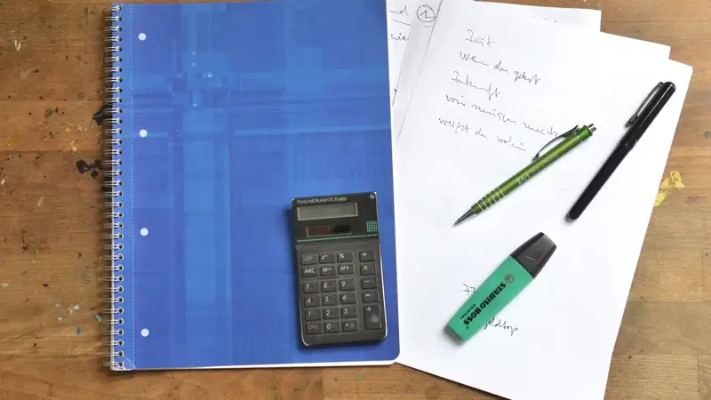 Notitieblok, rekenmachine en papieren op een houten bureau