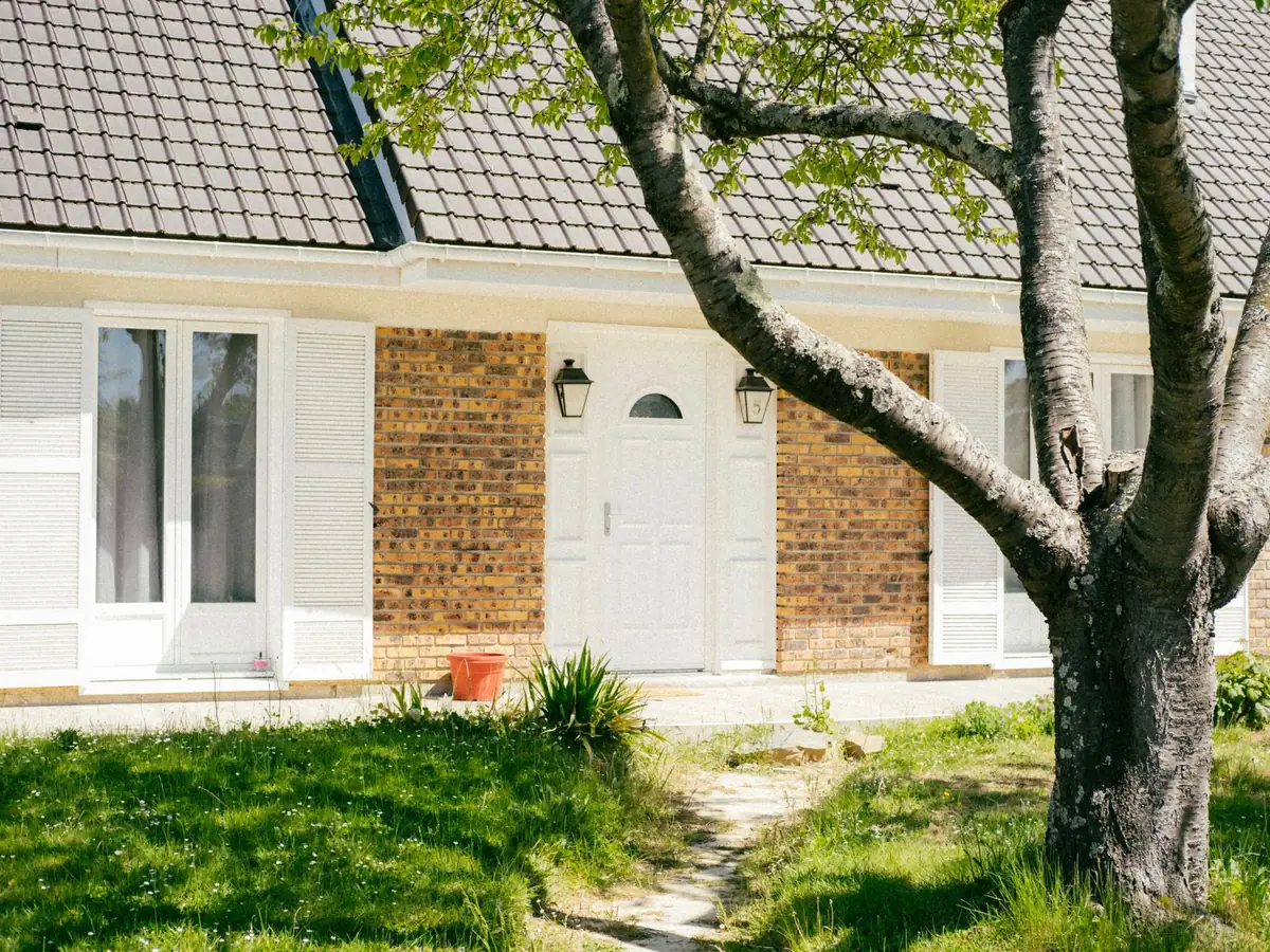 Bakstenen woning met witte luiken en een boom in de voortuin