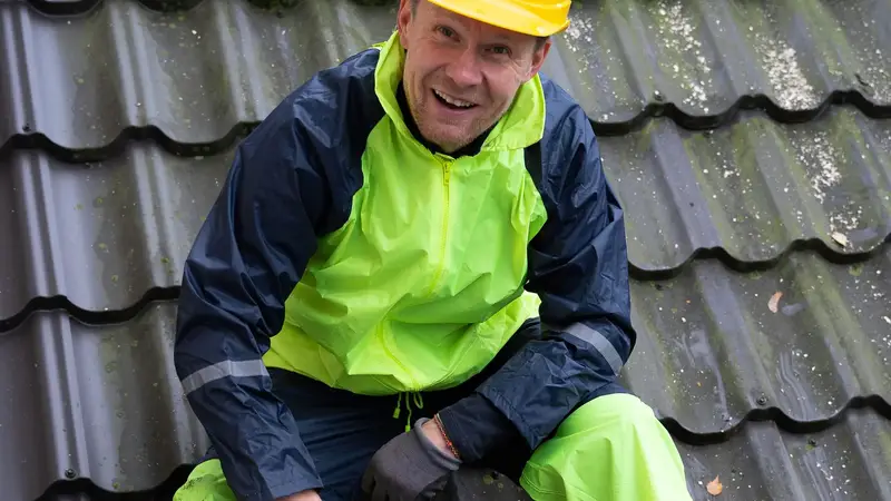 Dachdecker mit Helm schneidet Dachziegel auf dem Dach