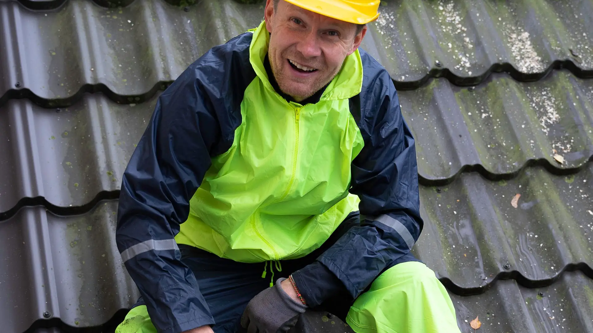 Dachdecker mit Helm schneidet Dachziegel auf dem Dach