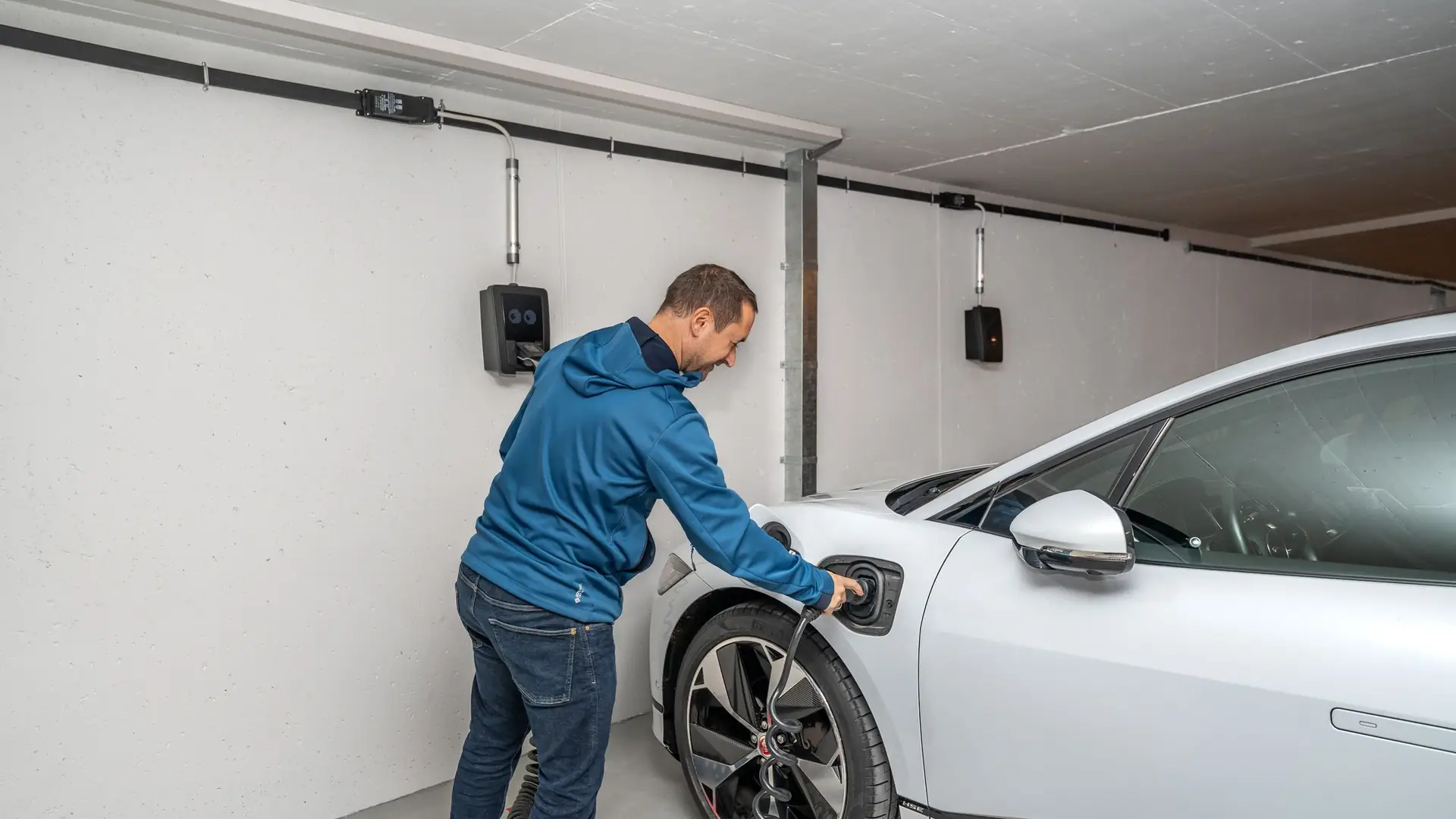 Mann steckt das Ladekabel einer Wallbox in ein Elektroauto in der Garage