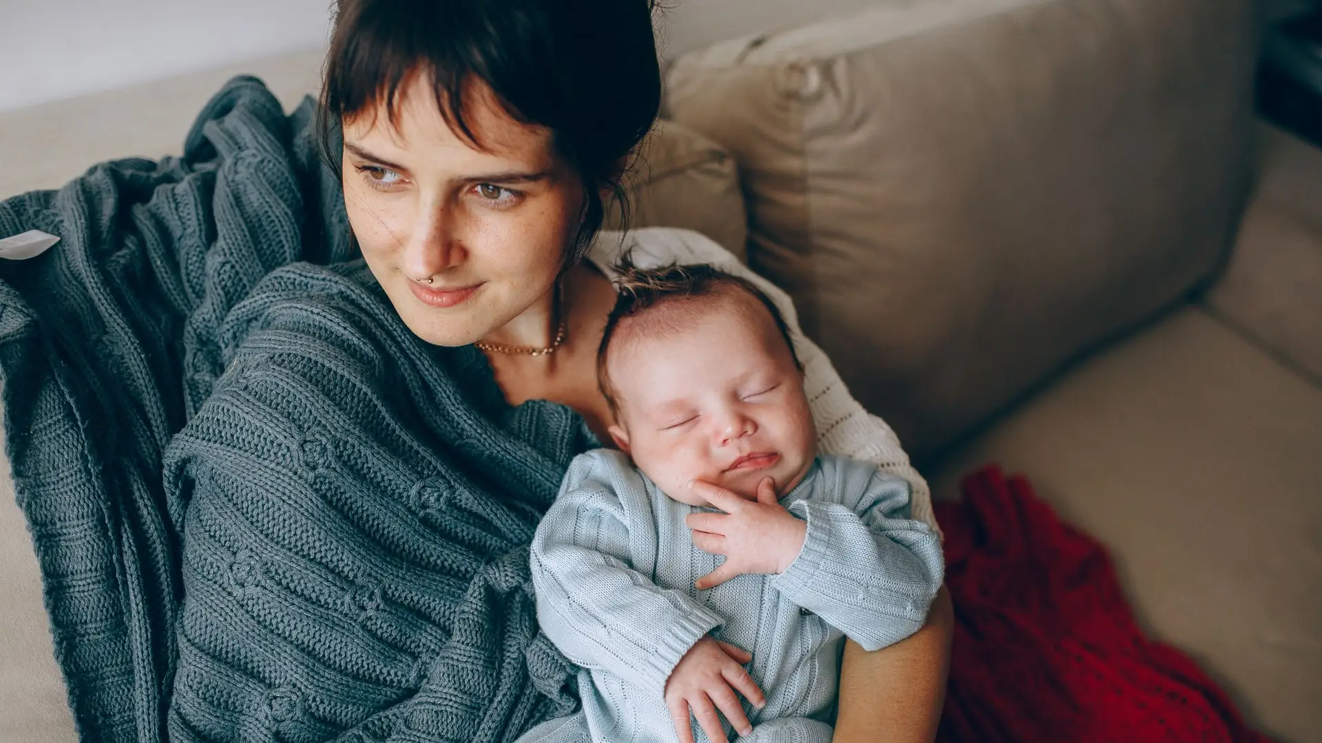 Mutter sitzt mit ihrem Baby im Arm auf dem Sofa