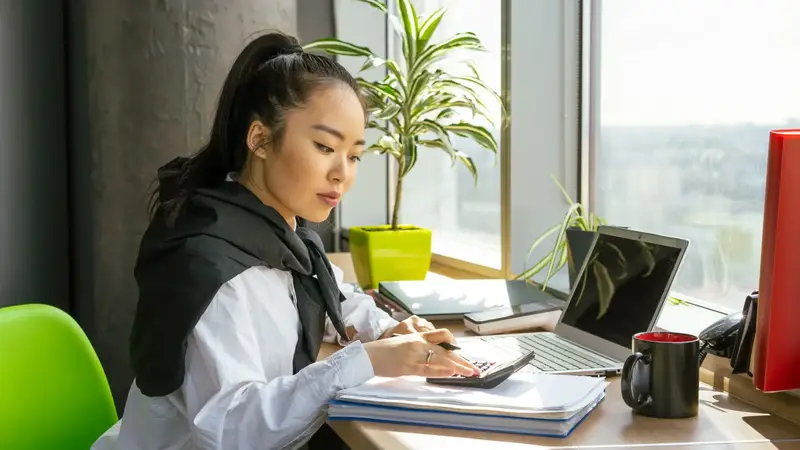Woman working through paperwork at a desk by the window