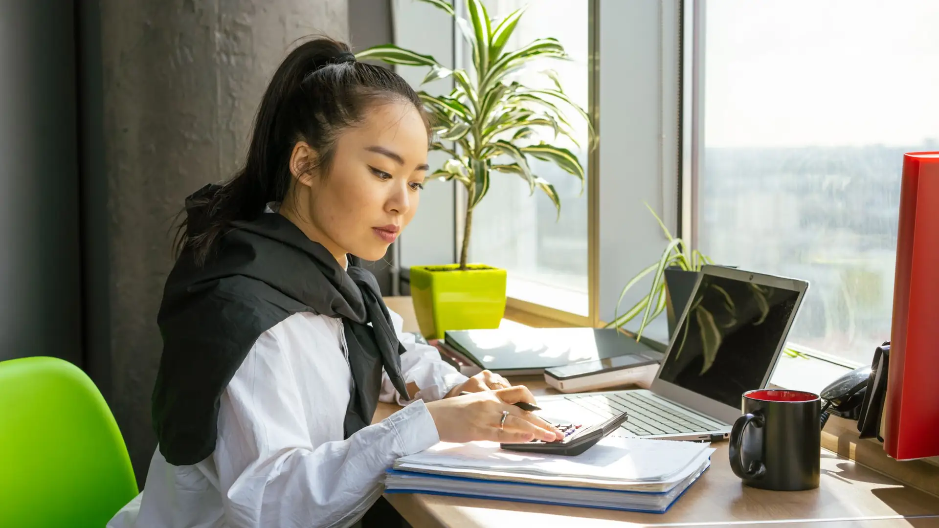 Woman working through paperwork at a desk by the window