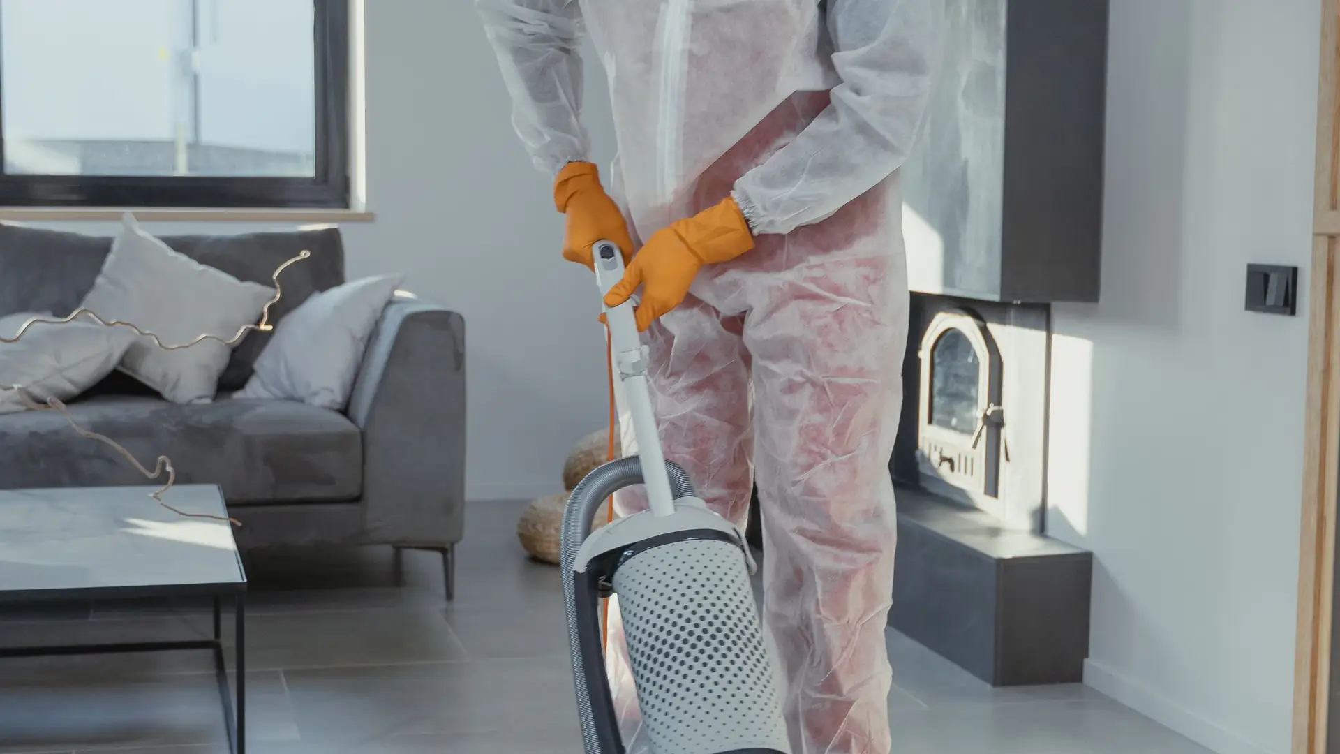 Cleaner in protective overalls hoovering a bright apartment
