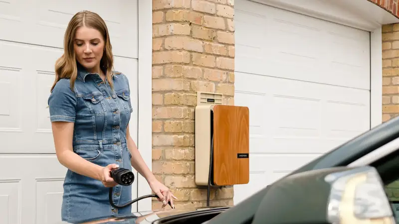 Woman plugging a charging cable into her car beside a wall charger