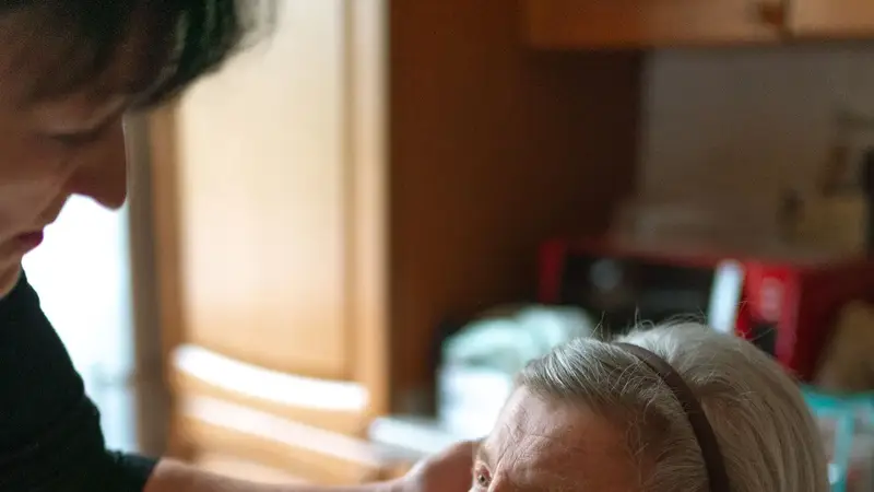 Wijkverpleegkundige legt geruststellend een hand op de wang van een oudere vrouw
