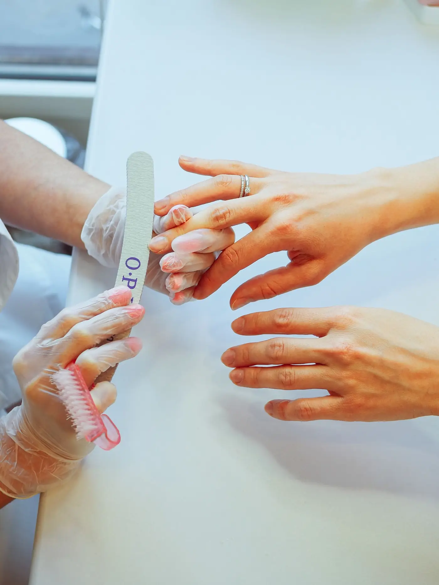 Two pairs of hands with a fresh manicure on a white table