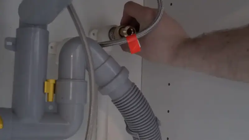 Plumber’s hand connecting a hose under a kitchen sink
